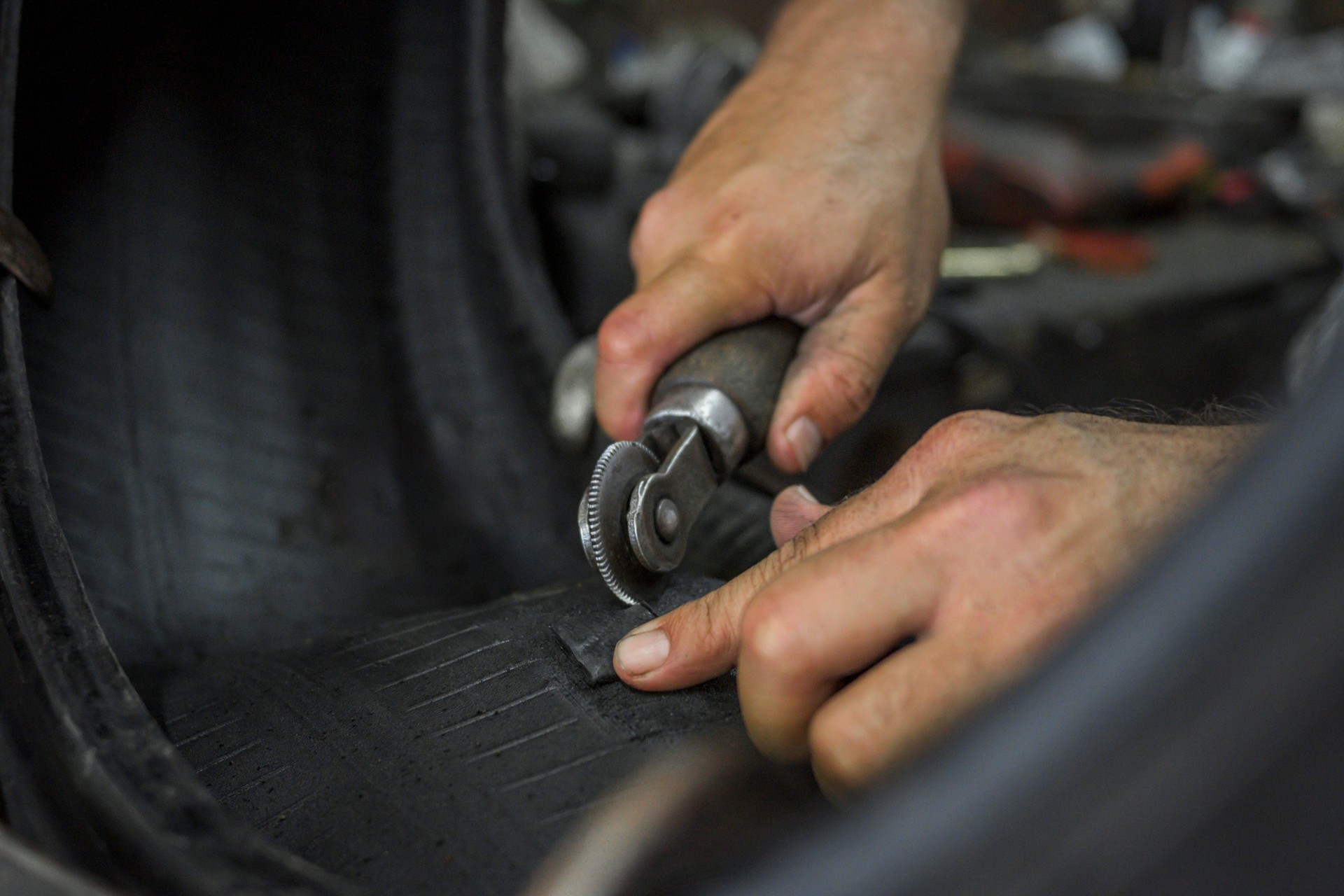close up hands of man grinding a tire with a manual roller to vulcanize the tire and patch it